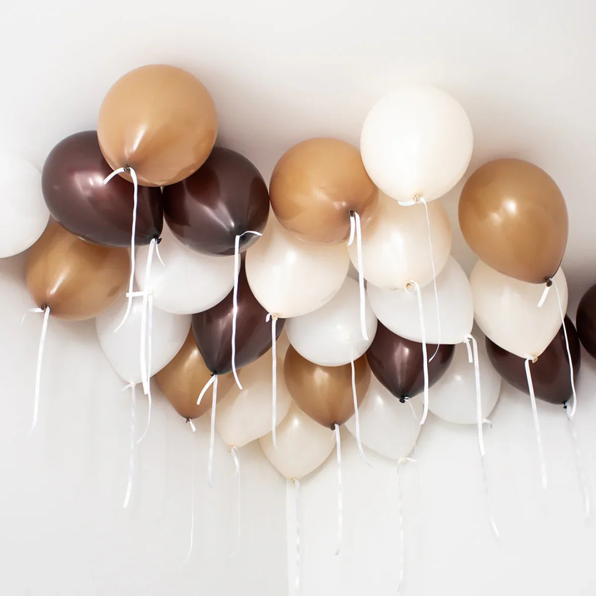 Ceiling decorated with helium balloons in neutral white, brown, and tan colors with white ribbons