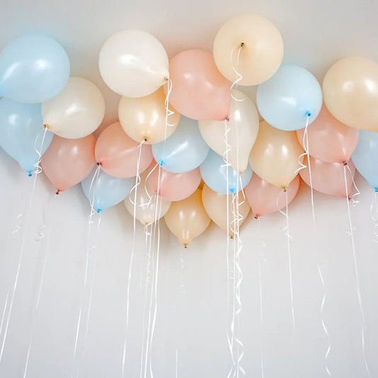 Helium balloons in neutral baby pink, blue, and cream colors floating on a white ceiling