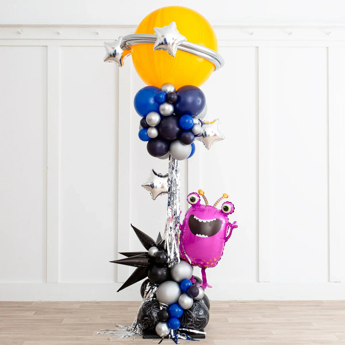 Outer space themed balloon pillar with yellow planet, silver stars, black and blue balloons, and pink alien balloon