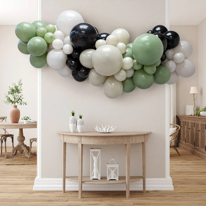 Green, black, white, and beige balloon garland above wooden console table in modern neutral living room