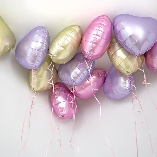 Helium pastel heart-shaped foil balloons in pink, purple, and gold floating on white ceiling