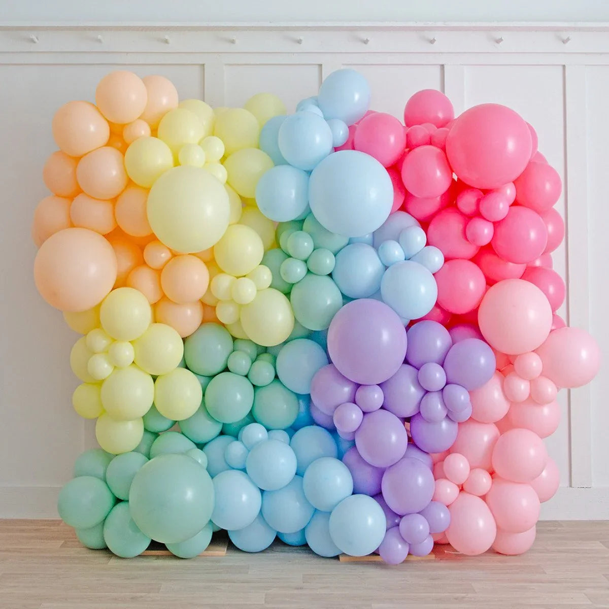 Large pastel rainbow balloon wall with clusters of different sized balloons against white paneled wall