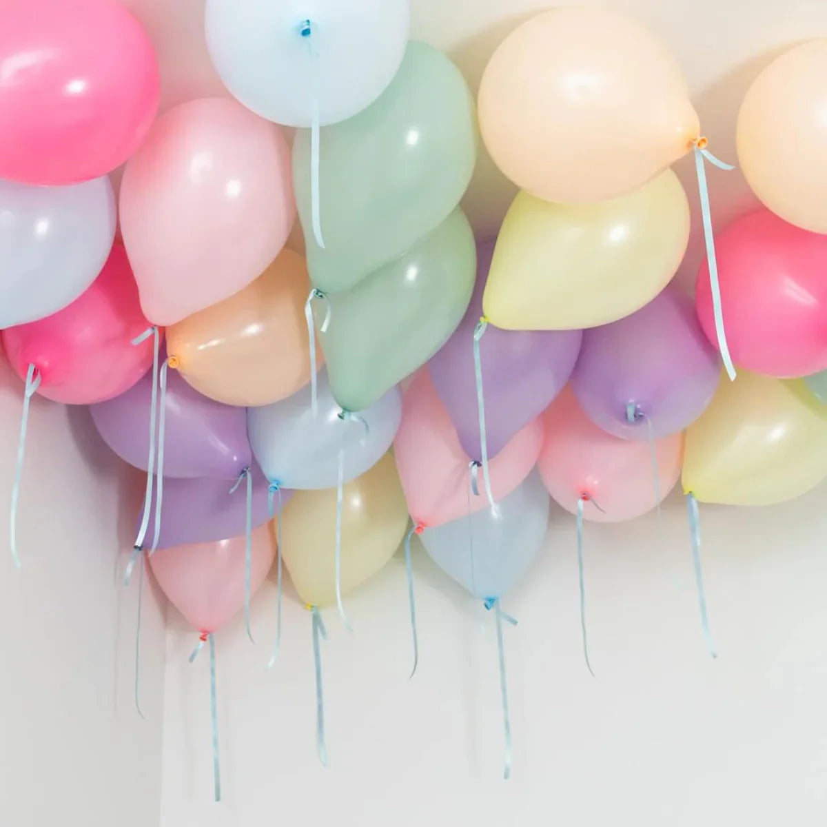 Cluster of pastel-colored helium balloons floating on a white ceiling with ribbons hanging down