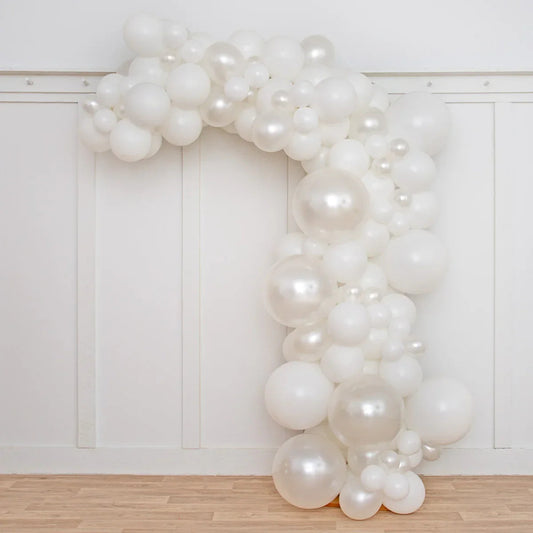 Asymmetric white and pearl balloon arch decoration against white paneled wall and wooden floor
