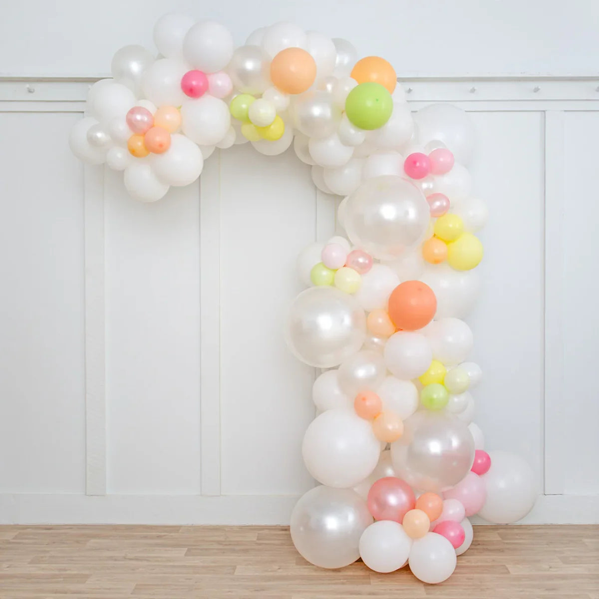 Asymmetric balloon arch with pearl white balloons and pastel accents in a bright room