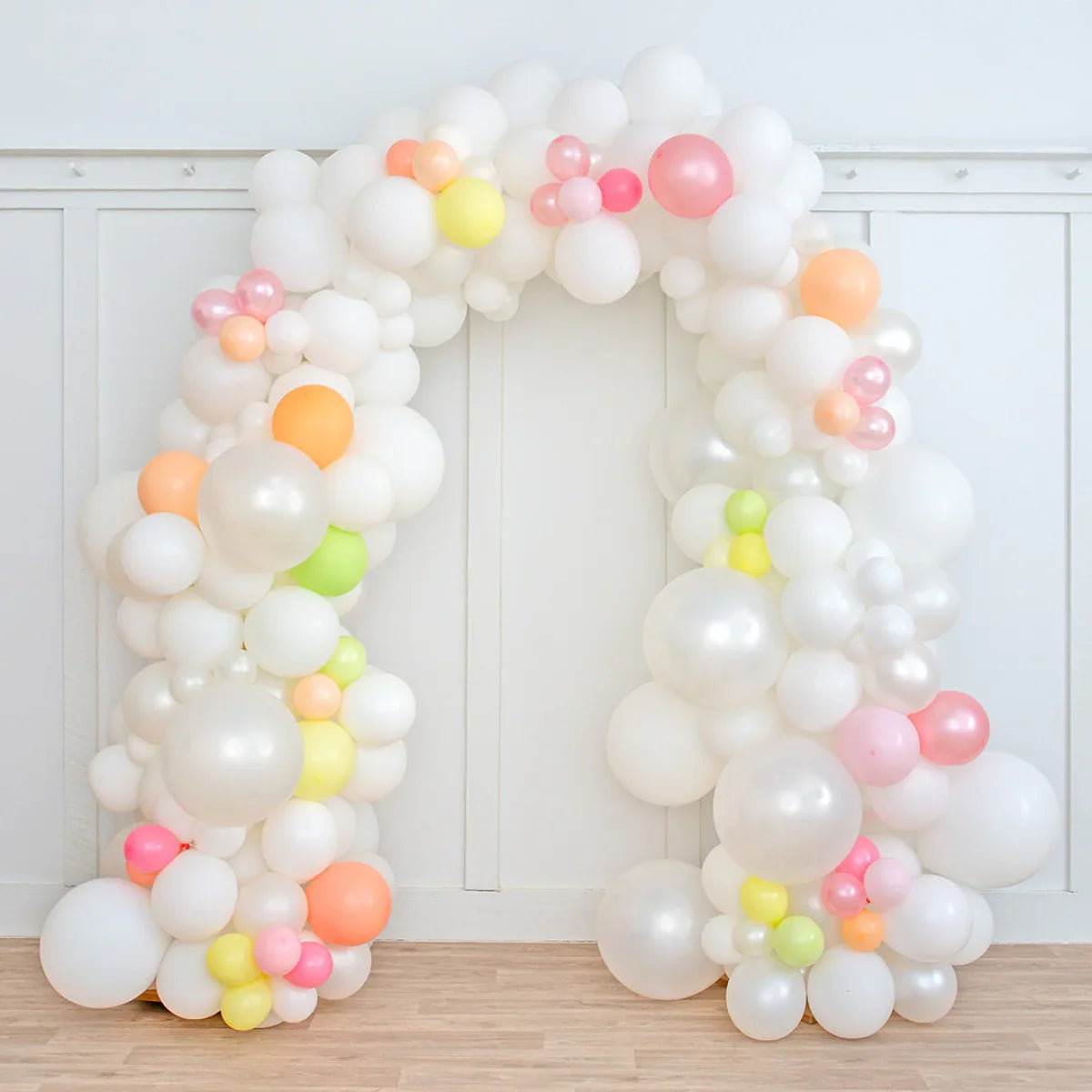 Pearl white balloon arch decorated with pastel pink, yellow, orange, and green balloons indoors