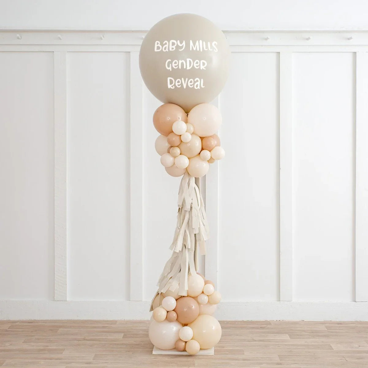 Neutral beige balloon pillar for baby gender reveal party with tassels and assorted balloons