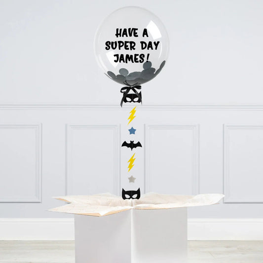 Personalised clear bubble balloon with black confetti, Batman masks, lightning bolts, and stars, reading 'Have a Super Day James'