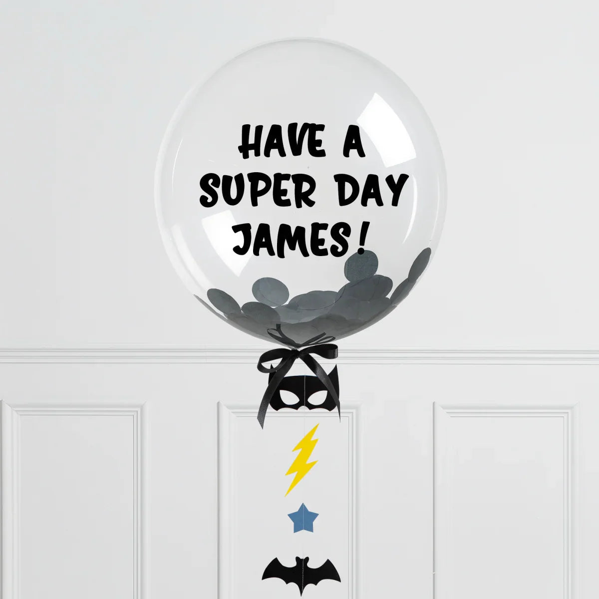 Clear personalized bubble balloon with black confetti and text 'Have a Super Day James!' with Batman-themed decorations