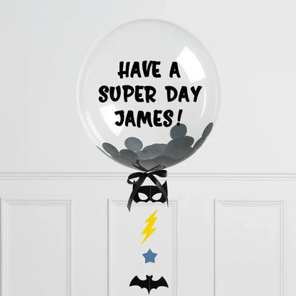 Clear personalized bubble balloon with black confetti and text 'Have a Super Day James!' with Batman-themed decorations