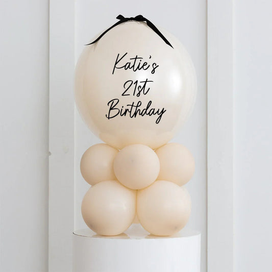 Ivory air-filled balloon stack with "Katie's 21st Birthday" text and black ribbon on top