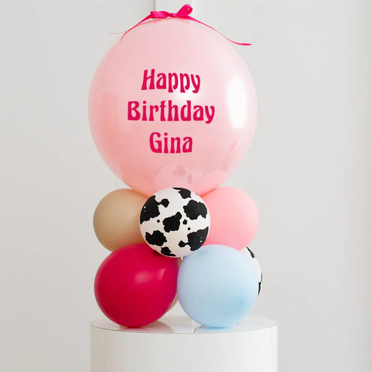 Personalised pink birthday balloon with message Happy Birthday Gina on bubble balloon stack with multi-colored and cow print balloons