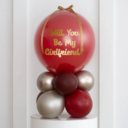 Personalised deep red pearl balloon with gold text 'Will You Be My Girlfriend?' and decorative balloon cluster