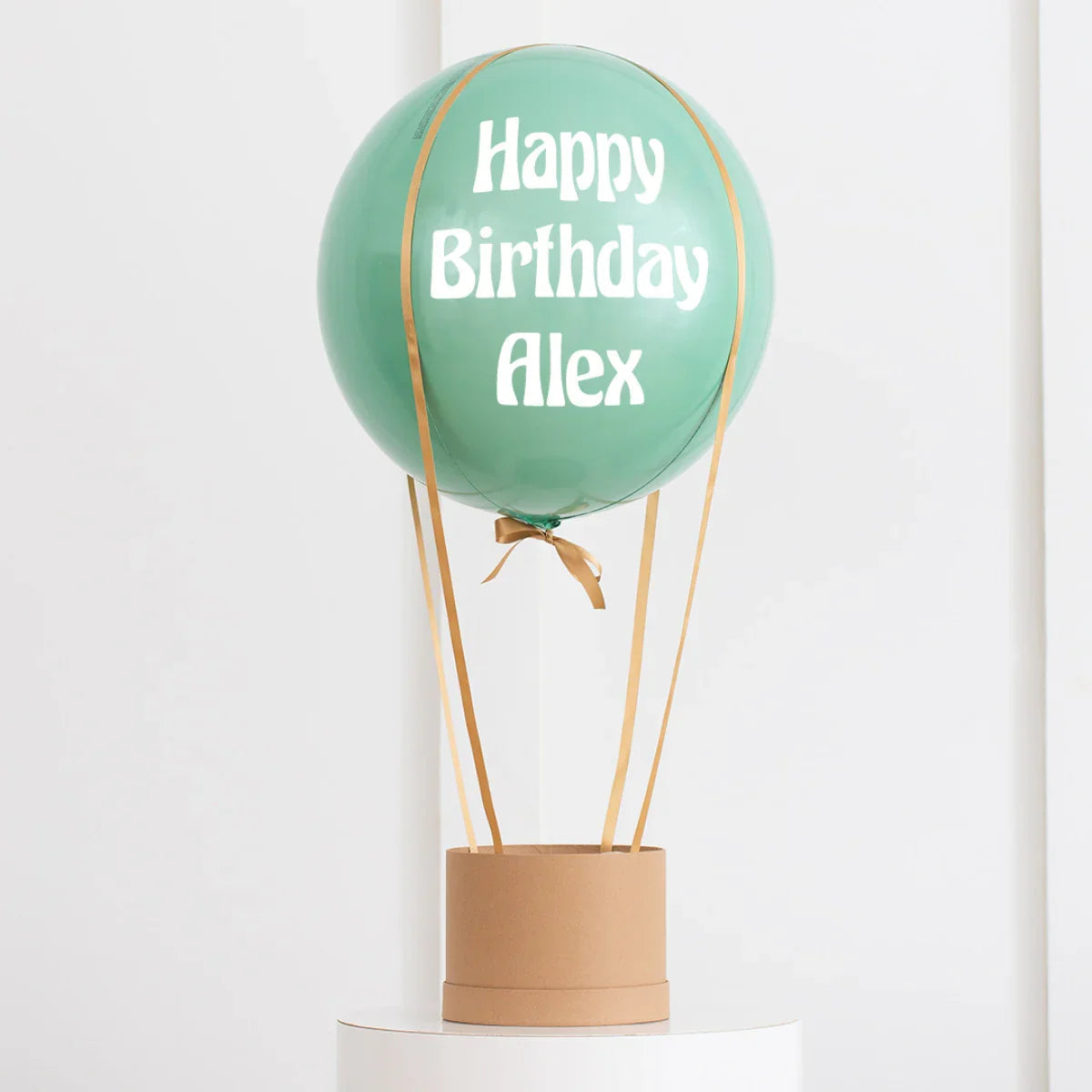 Personalised eucalyptus green hot air balloon balloon with 'Happy Birthday Alex' text, gold ribbons, and a brown base