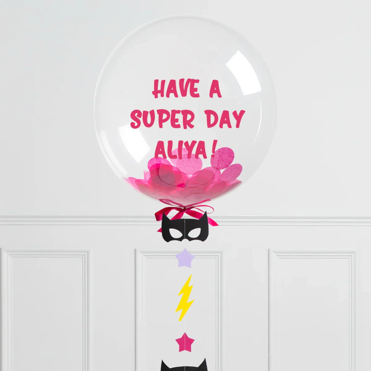 Clear bubble balloon with pink confetti and message Have a super day Aliya with black mask and colorful decorations
