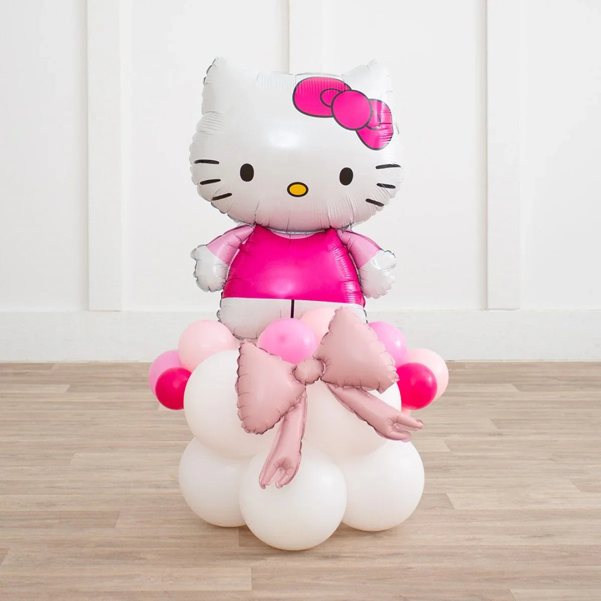Hello Kitty foil balloon on a base of white and pink latex balloons with a large pink bow, standing on wooden floor