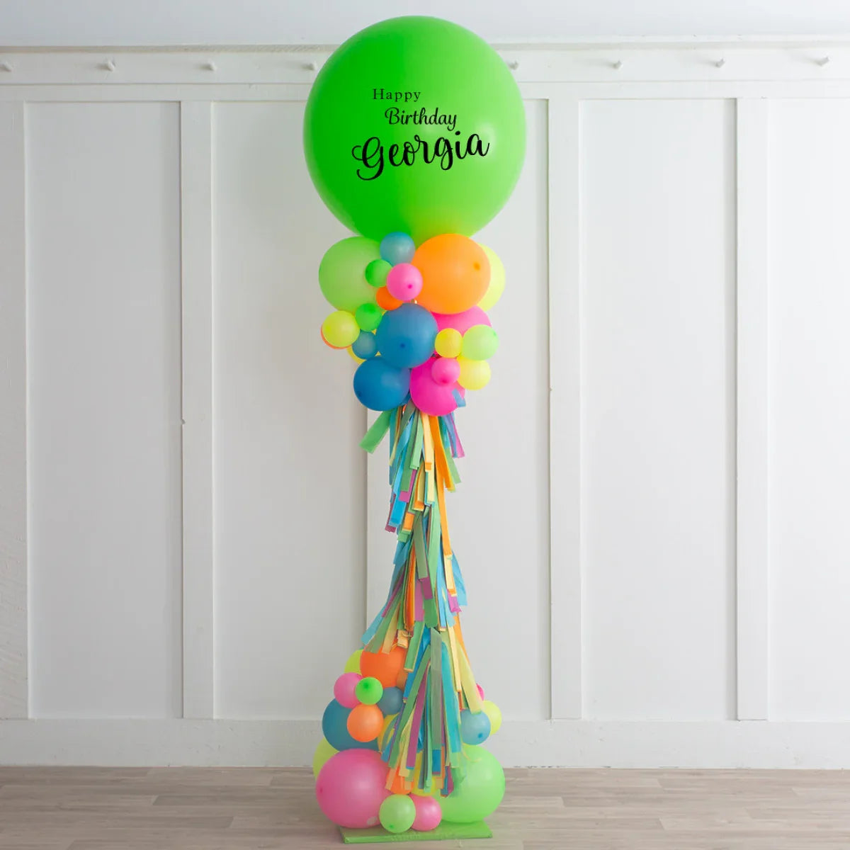 Colorful birthday balloon pillar with green top balloon reading Happy Birthday Georgia, decorated with vibrant balloons and tassels
