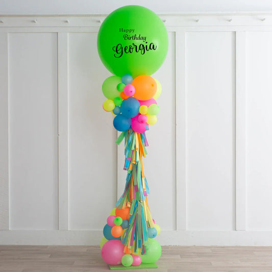 Colorful birthday balloon pillar with green top balloon reading Happy Birthday Georgia, decorated with vibrant balloons and tassels