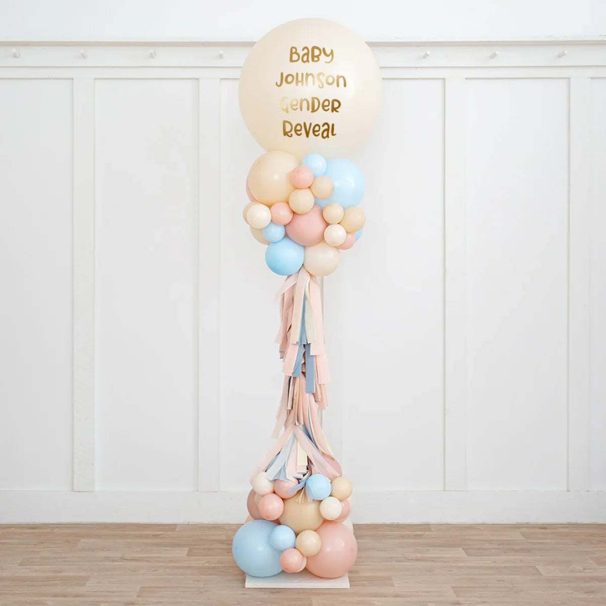 Personalized neutral pink and blue balloon pillar for baby gender reveal party in a white room