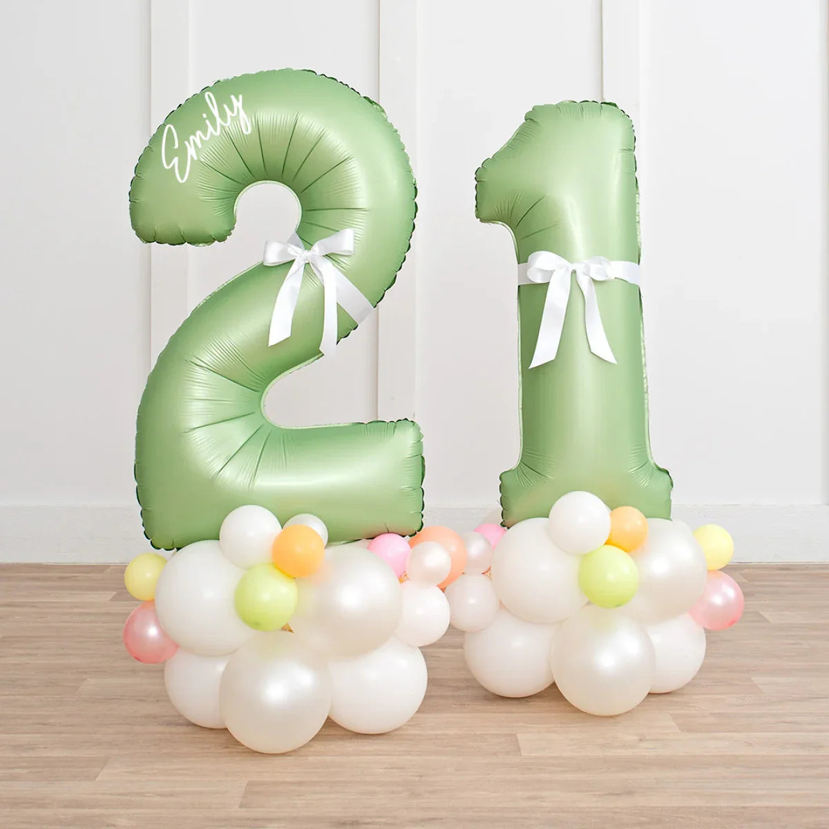 Green number 21 balloons with white bow and white and pastel balloon clusters on wooden floor