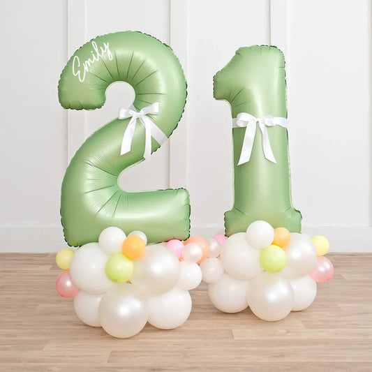 Green number 21 balloons with white bow and white and pastel balloon clusters on wooden floor