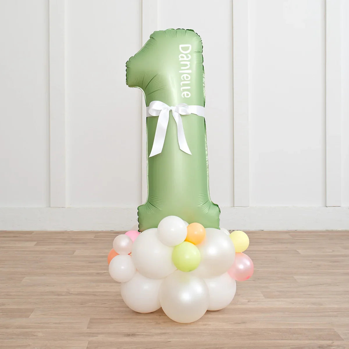 Personalized pastel green number 1 balloon with white bow and colorful balloon cluster on wooden floor