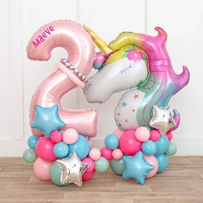 Personalized pink number 2 and colorful unicorn foil balloon with star-shaped and round balloons on wooden floor