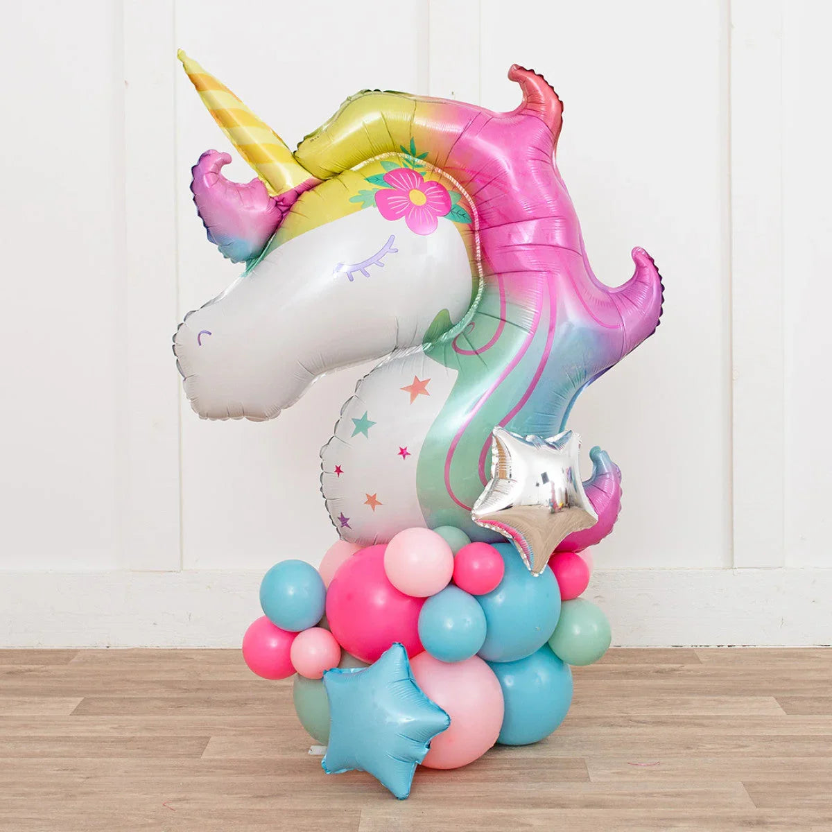 Colorful unicorn foil balloon with pastel pink, blue, and green latex balloons base on wood floor