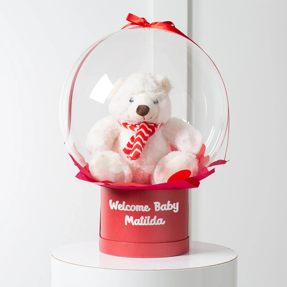 White plush polar bear with red patterned scarf inside clear bubble on red base saying Welcome Baby Matilda