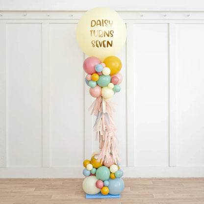 Personalised pastel balloon pillar with gold text 'Daisy Turns Seven' for birthday party decoration