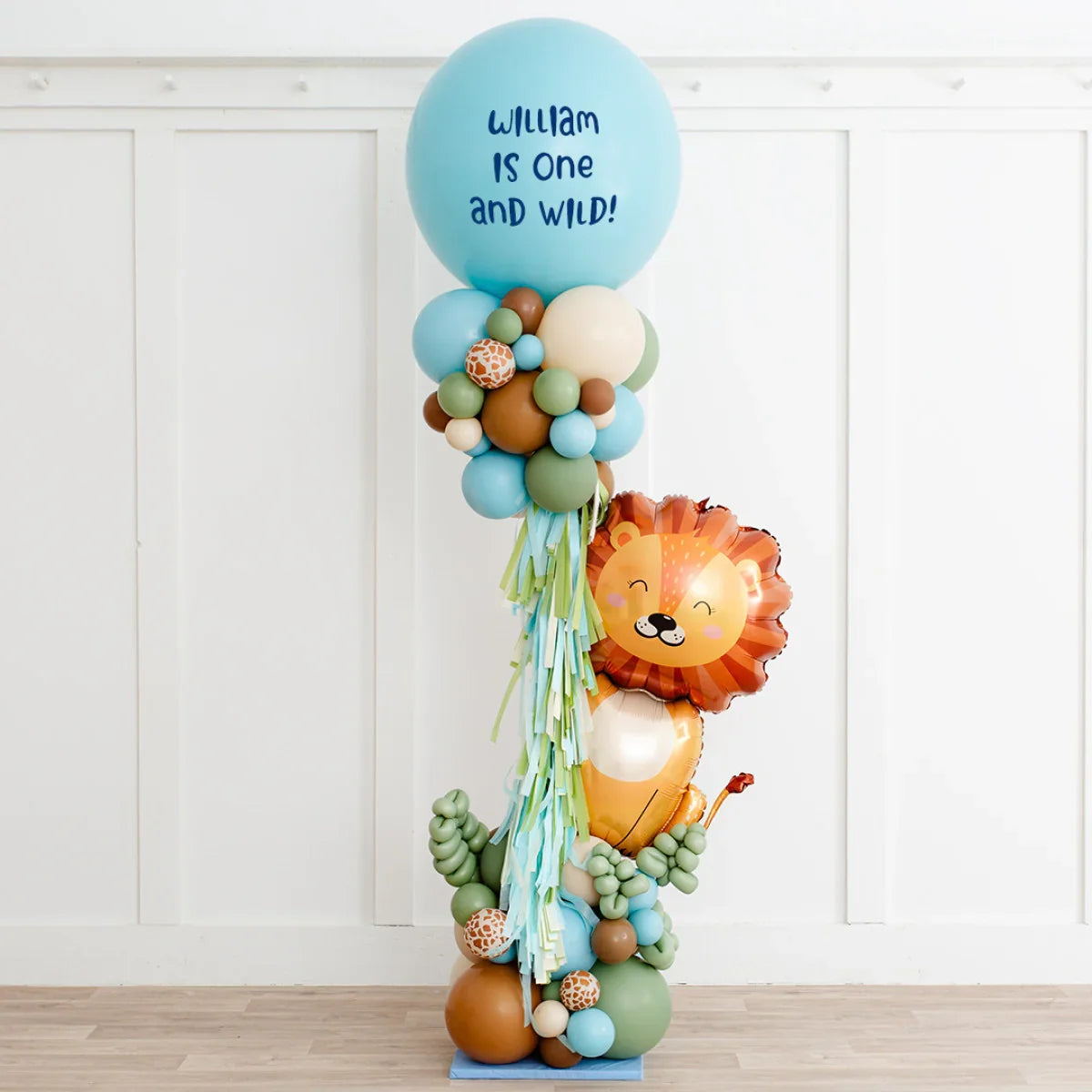Safari-themed balloon pillar with blue top balloon reading 'William is one and wild' and lion-shaped balloon