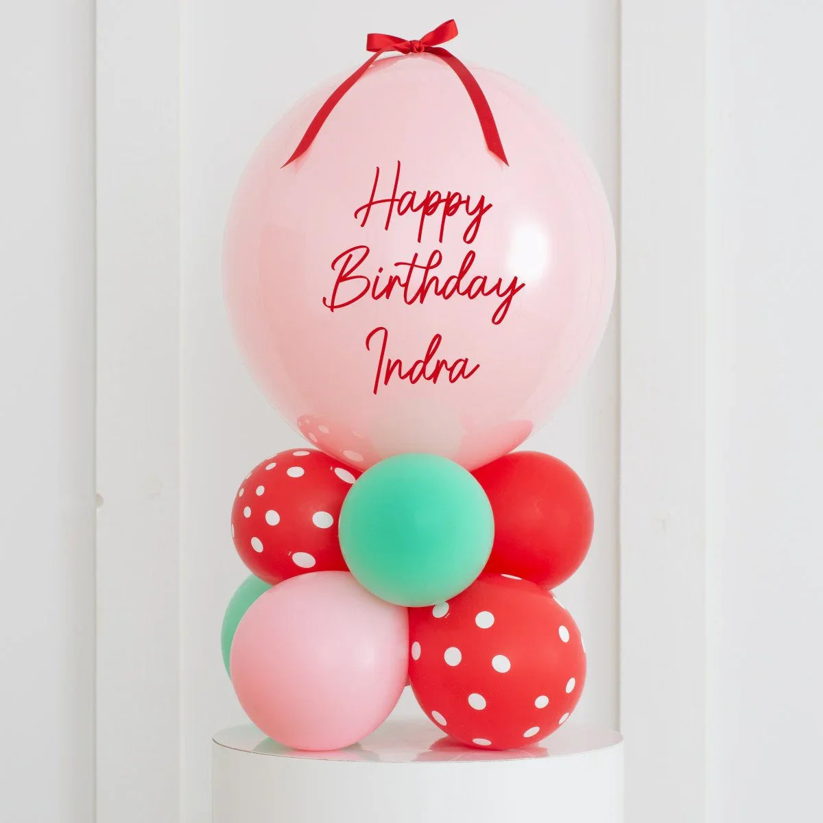 Personalized pink birthday balloon stack with red ribbon and mixed green, red, polka dot balloons