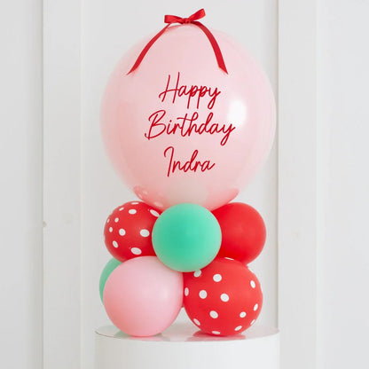 Personalized pink birthday balloon stack with red ribbon and mixed green, red, polka dot balloons