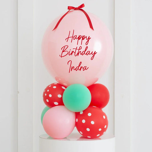 Personalized pink birthday balloon stack with red ribbon and mixed green, red, polka dot balloons