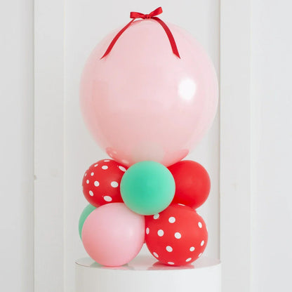 Decorative balloon stack with large pink balloon topped by red bow, surrounded by red, green, and polka dot balloons