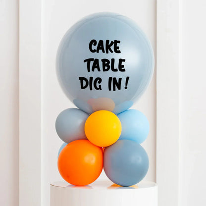 Colorful balloon stack with grey, orange, and yellow balloons and 'CAKE TABLE DIG IN!' text on top balloon
