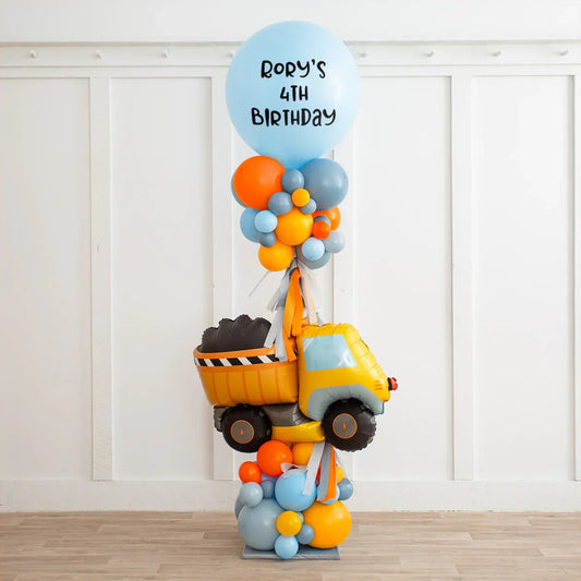 Colorful birthday balloon arrangement with orange, blue, gray clusters and a yellow dump truck balloon