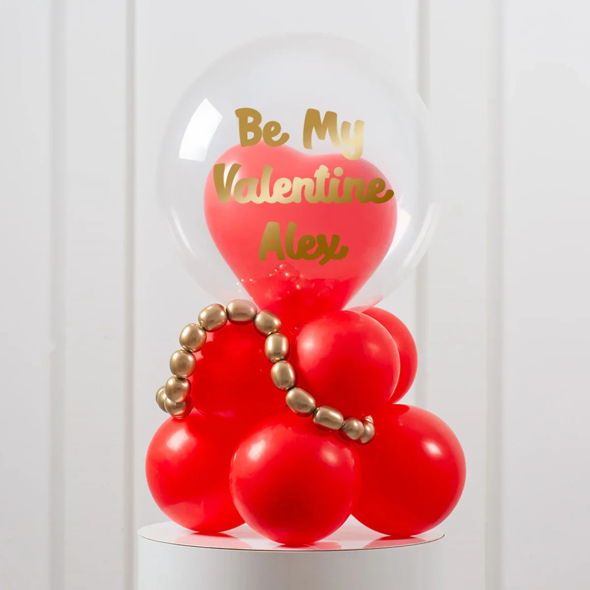 Valentine's Day balloon arrangement with red heart-shaped and round balloons, gold beads, and personalized gold text