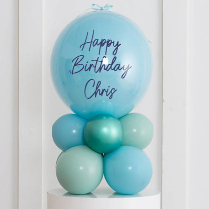Personalized blue birthday balloon stack with Happy Birthday Chris text on air-filled bubbles