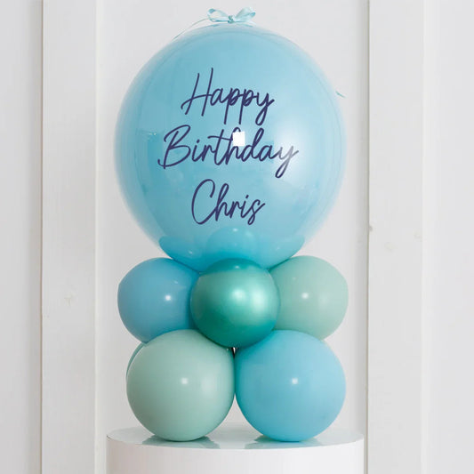 Personalized blue birthday balloon stack with Happy Birthday Chris text on air-filled bubbles