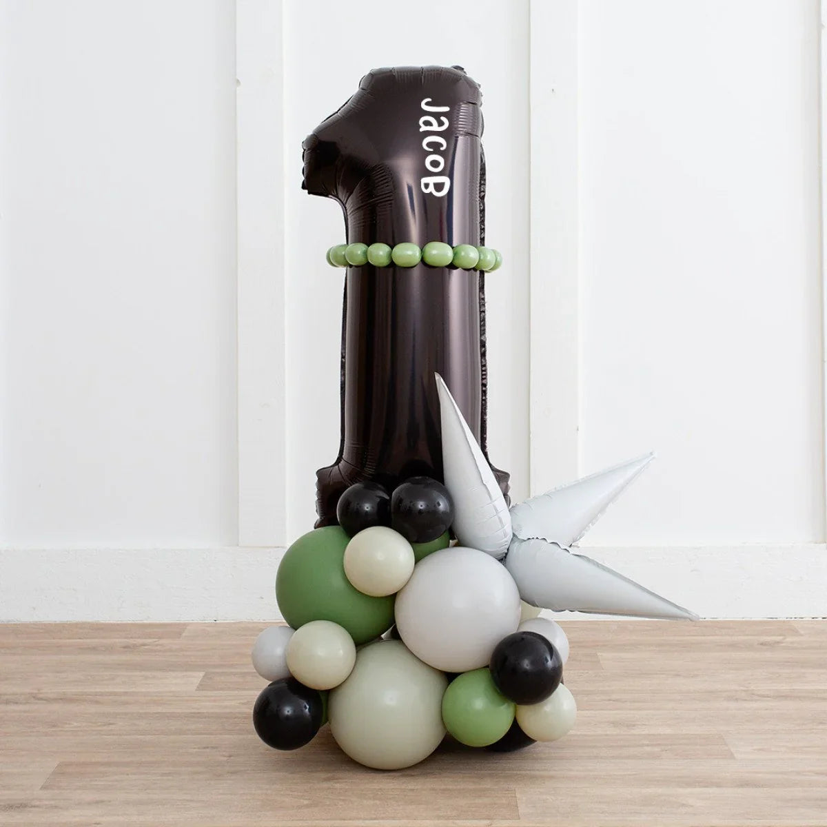 Black number 1 balloon with name Jacob, surrounded by green, white, and black balloons and silver spikes on wooden floor