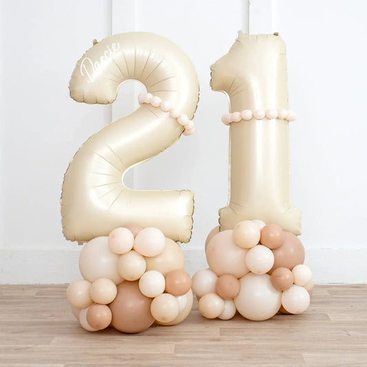 Beige and neutral color inflated number 21 balloon stack with small balloons base and decorations on wooden floor
