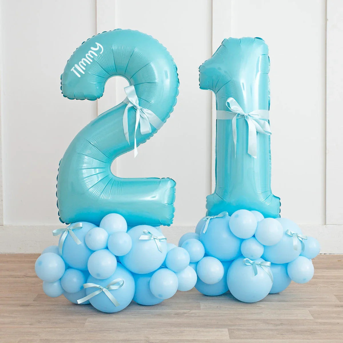 Blue number 21 balloon display with personalized name Timmy and baby blue bow clusters on wooden floor
