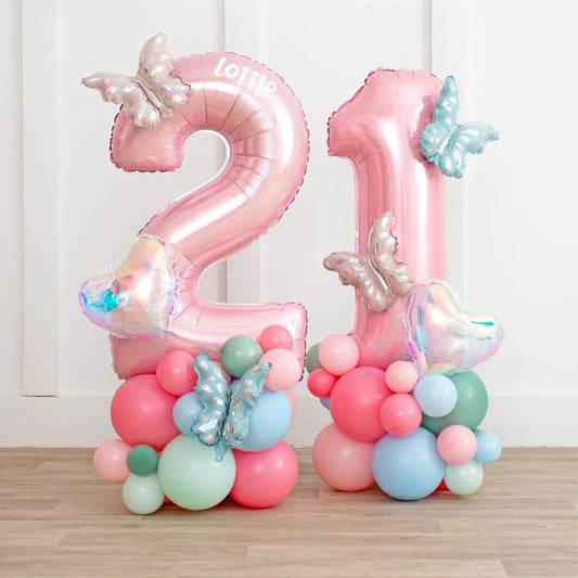 Pink number 21 birthday balloon stack with pastel butterfly and heart-shaped foil balloons on wooden floor