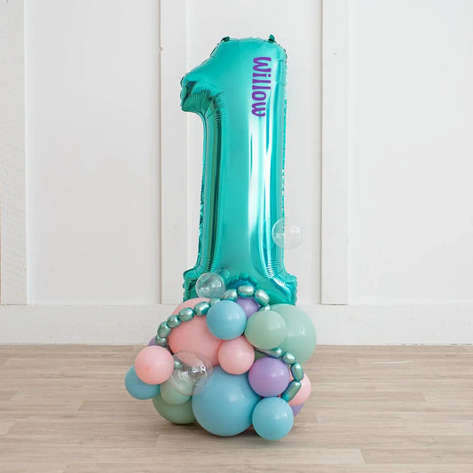 Teal number 1 foil balloon with the name Willow, decorated with pastel and clear balloons on a wooden floor