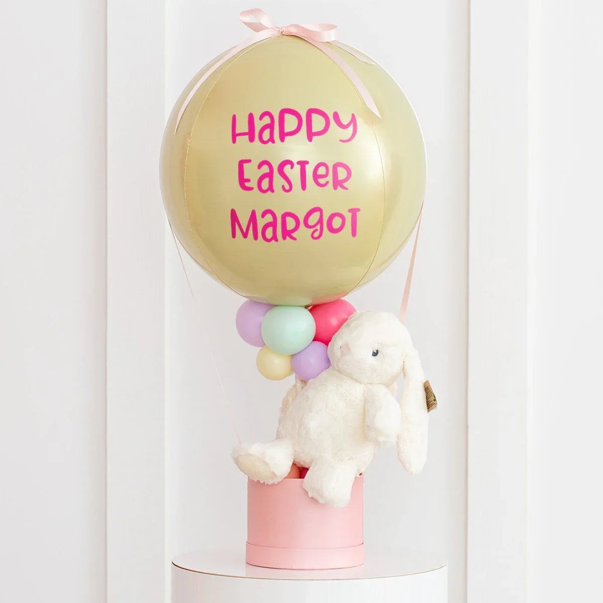Easter-themed balloon decoration with personalized text, pastel balloons, and white plush bunny in pink box