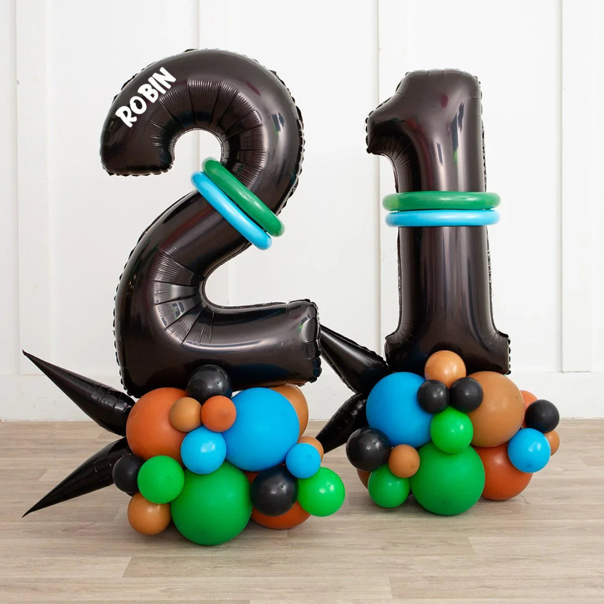 Black number 21 balloons with green and blue rings, supported by colorful cluster balloons on wooden floor