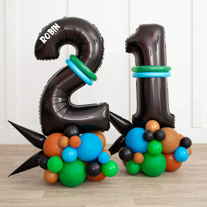Black number 21 balloons with green and blue rings, supported by colorful cluster balloons on wooden floor