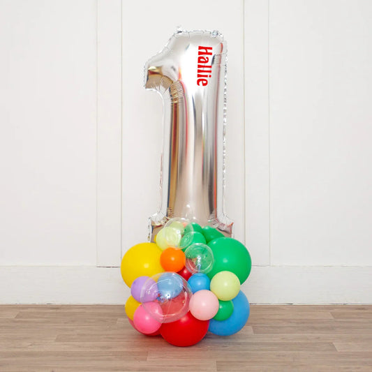 Silver number 1 balloon with name Hallie and colorful balloon cluster on wooden floor