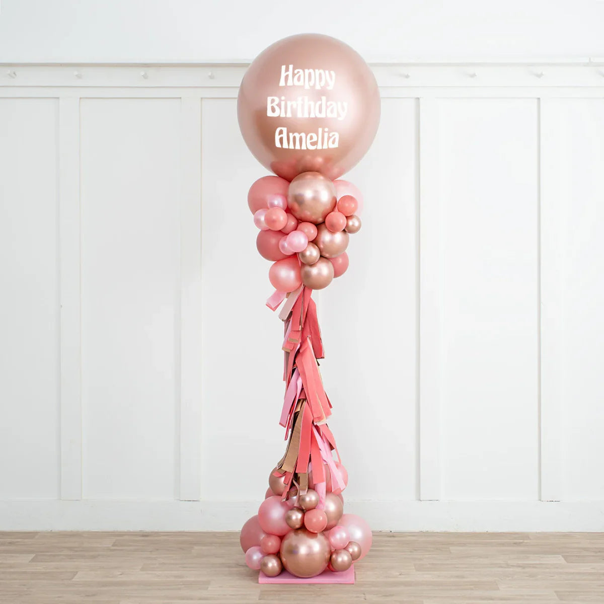 Rose gold and blush pink personalized birthday balloon pillar with Happy Birthday Amelia text